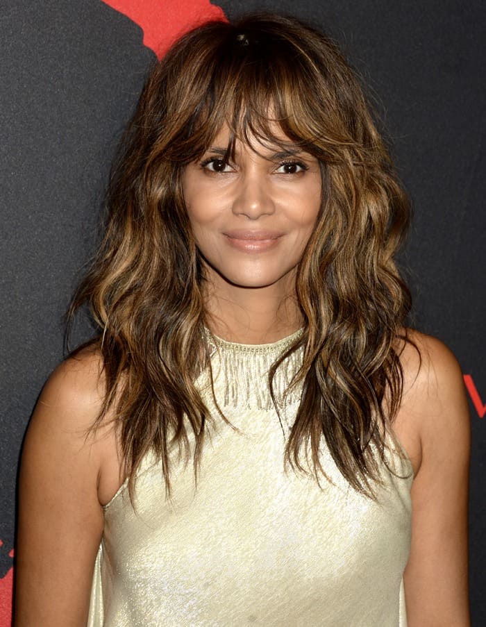 Halle Berry stuns with her voluminous waves and subtle, glowing makeup, perfectly complementing her shimmering gold outfit