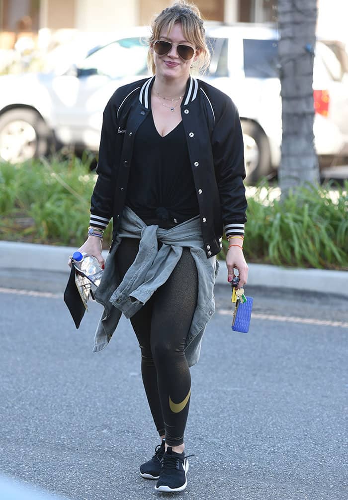 Hilary Duff steps out in a laid-back, sporty look with a black v-neck tee, Nike leggings, and an R13 baseball jacket, finishing off with her Nike Juvenate sneakers and aviator sunglasses