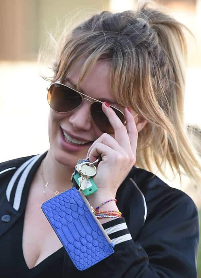 In addition to her Ray-Ban aviator sunglasses and keys, Hilary Duff is also wearing several colorful beaded bracelets on her wrist and holding a vibrant blue snakeskin-textured cardholder attached to her keys
