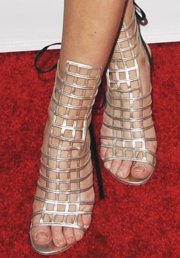 A close-up highlights Zara’s metallic lattice-strap heels, their geometric cage design adding shine and structure against the red carpet