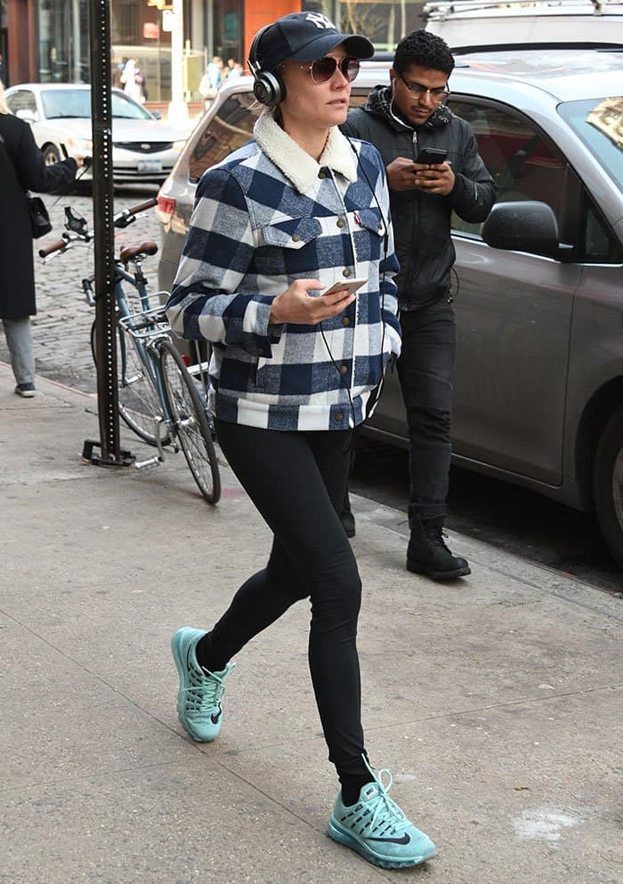 Replicate Diane Kruger’s effortless NYC street style with a plaid sherpa jacket, black leggings, Nike Air Max sneakers, a Yankees baseball cap, and aviator sunglasses