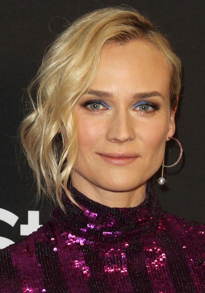 Diane Kruger exudes retro glam with a wavy side-swept hairstyle, metallic blue smoky eye makeup, and pearl-accented Alina Abegg 'Saturnation' hoop earrings