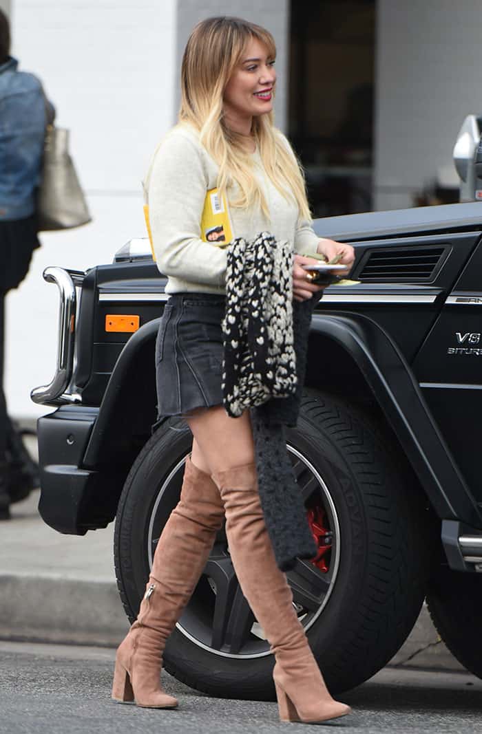 To replicate Hilary Duff's outfit, pair a cream sweater with a black denim mini skirt and complete the look with suede knee-high boots and a cozy scarf for a versatile and stylish ensemble