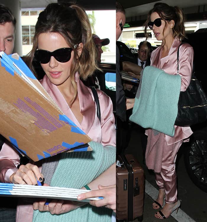 Kate Beckinsale embraces effortless airport chic in a blush satin pajama-style ensemble, paired with Francesco Russo sandals, Oliver Goldsmith sunglasses, and a cozy mint green blanket draped over her arm