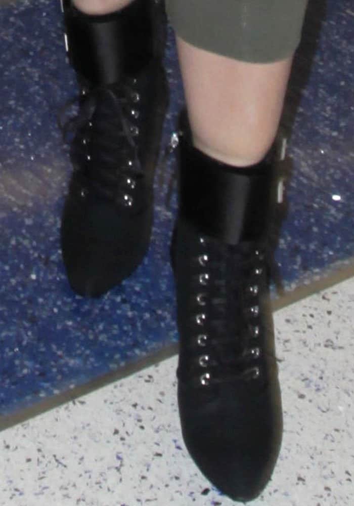 Khloé Kardashian stepped out in sleek black Balmain lace-up boots featuring silver eyelets and a pointed toe, adding an edgy touch to her chic airport look