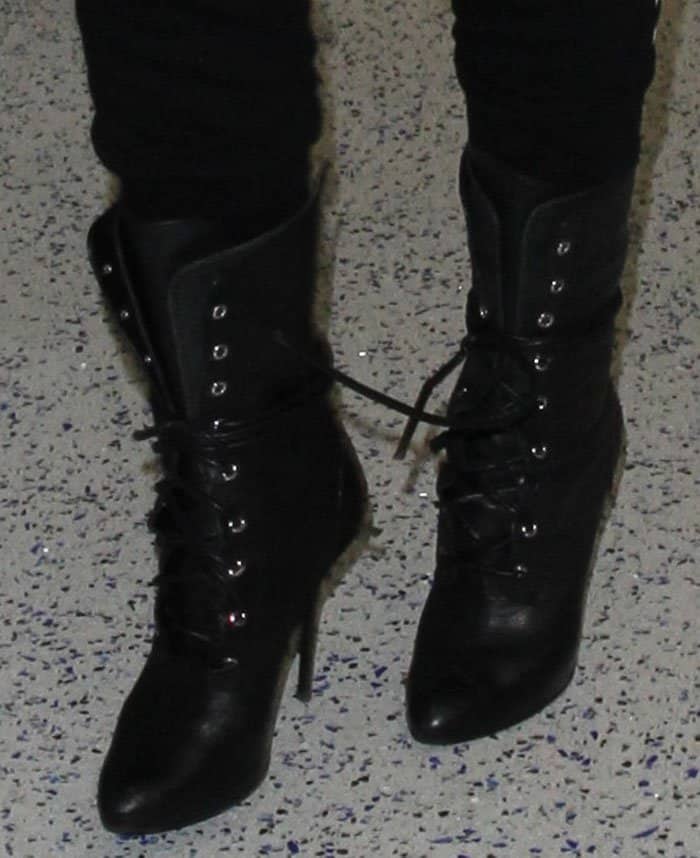 Khloé Kardashian's sleek black leather lace-up boots with stiletto heels add a bold, edgy touch to her casual airport ensemble