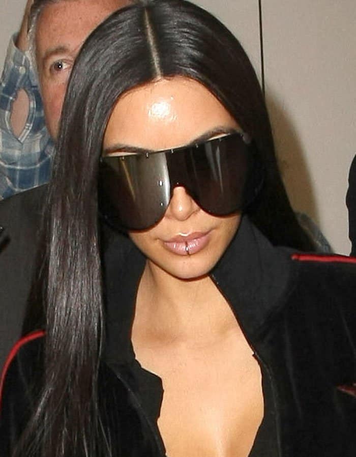 Kim Kardashian spotlights a faux lip ring while arriving at LAX in oversized Rick Owens shield sunglasses