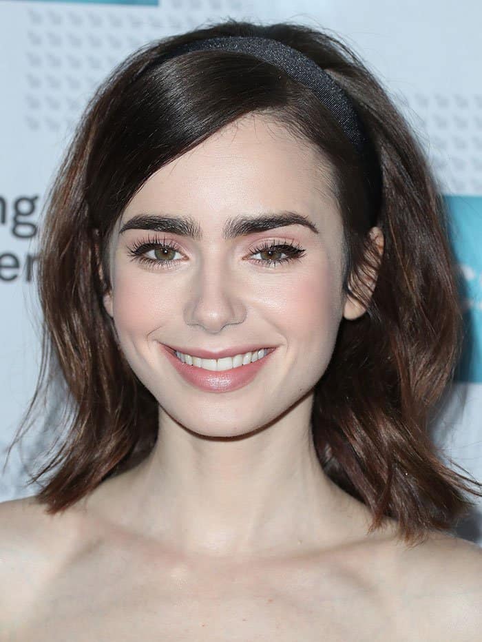 Lily Collins radiates timeless charm with soft waves styled under a sleek black headband, perfectly framing her glowing smile