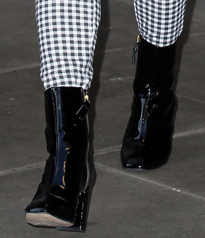 Maisie Williams completes her outfit with glossy patent ankle boots, featuring sleek side zips, square toes, and a sturdy four-inch heel for a modern yet polished finish