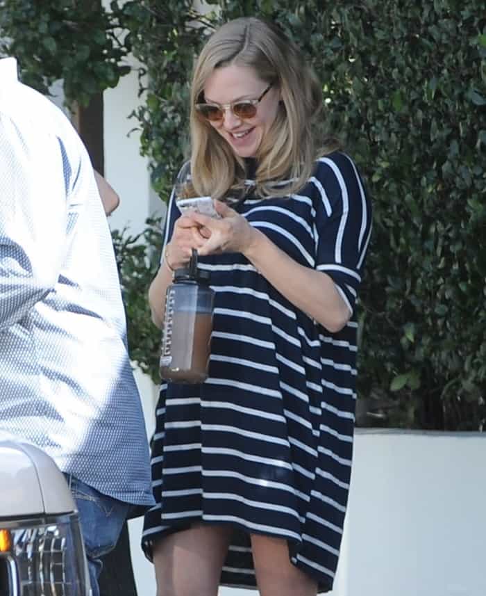 Amanda Seyfried beams in a navy striped maternity dress, accessorized with chic aviator sunglasses and her signature loose waves, while holding a sleek water bottle