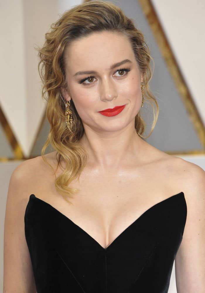 Brie Larson completed her Oscars look with soft, side-swept waves, glowing golden eye makeup, and a bold red lip that added classic Hollywood polish to her black velvet gown