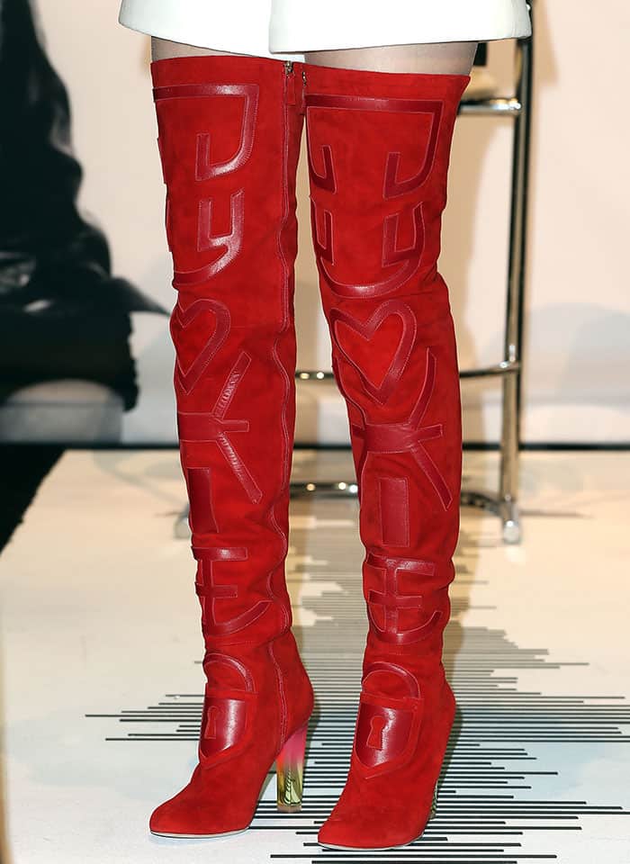 The Schiaparelli thigh-high boots feature suede construction with appliquéd lettering and a sculptural silhouette that extends well above the knee