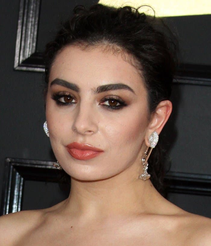 Charli XCX exudes confidence as she pairs her dramatic smoky eyes and glossy nude lips with the striking Vivienne Westwood safety pin earrings, showcasing how edgy accessories can elevate a classic red carpet beauty look