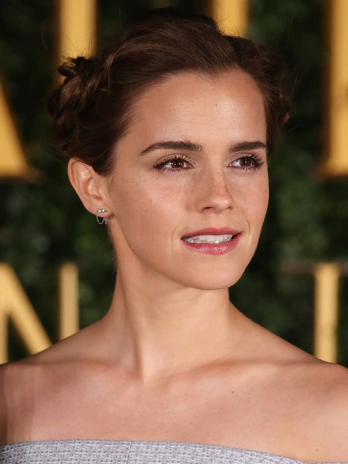 Emma Watson styled her hair in elegant milkmaid braids, paired with delicate diamond stud earrings, adding a touch of timeless sophistication