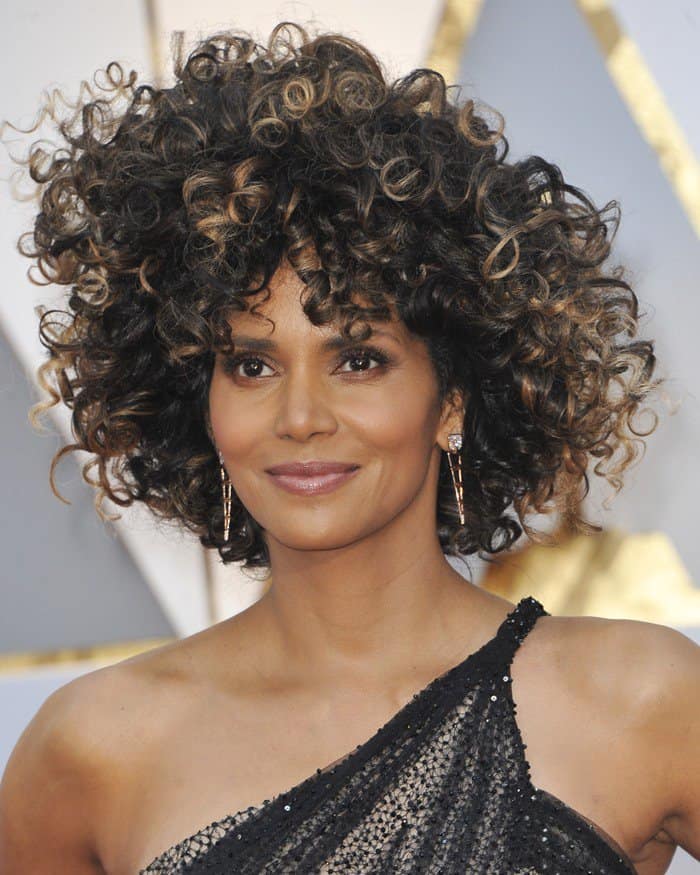 Halle Berry embraces her natural curls in a bold and voluminous hairstyle, complementing her one-shoulder Atelier Versace gown