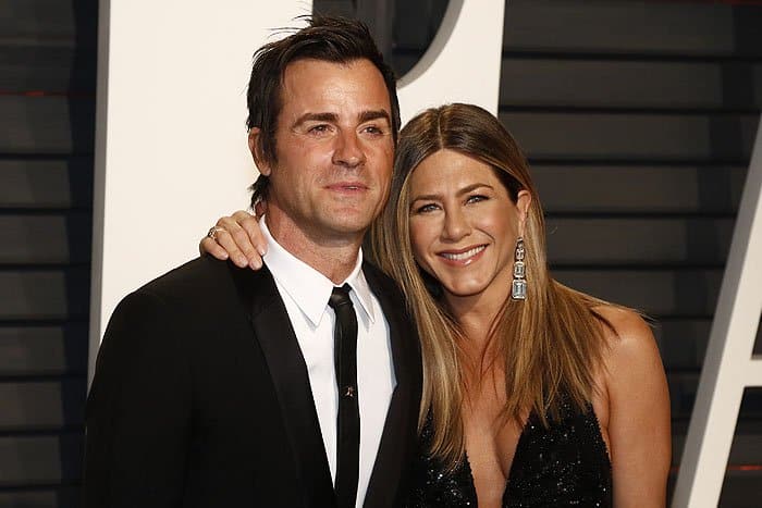 Jennifer Aniston and Justin Theroux pose together, with Jennifer wearing diamond Lorraine Schwartz earrings and a black Versace gown