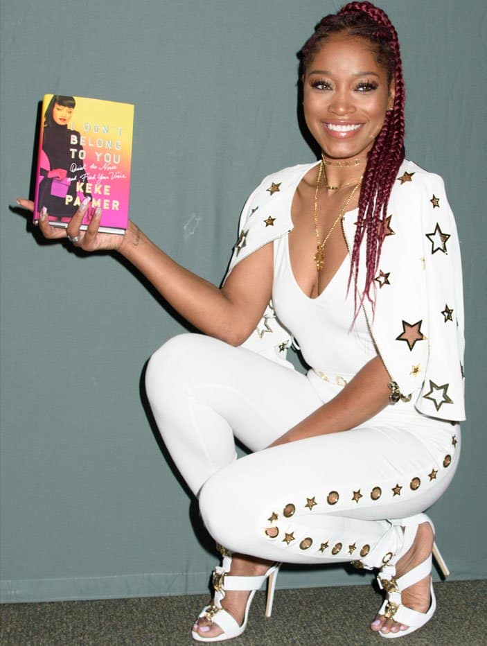 Keke Palmer poses with her book while showcasing her star-studded Philipp Plein ensemble and matching white gladiator heels