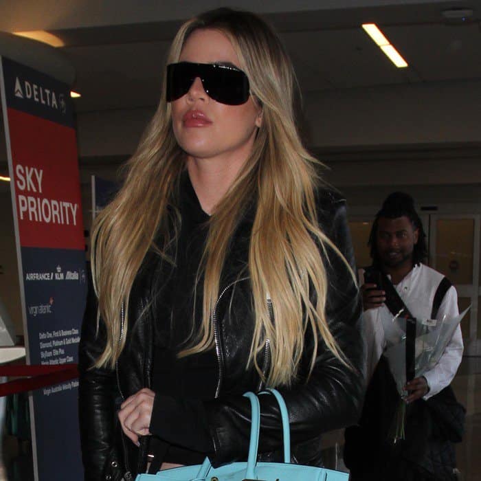 Khloé Kardashian looks effortlessly chic in a black leather jacket, oversized sunglasses, and a light blue Hermès Birkin bag at the airport