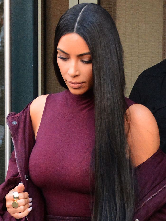 Kim Kardashian stuns with sleek, waist-length straight hair and a sharp center part, complementing her monochromatic burgundy Yeezy ensemble