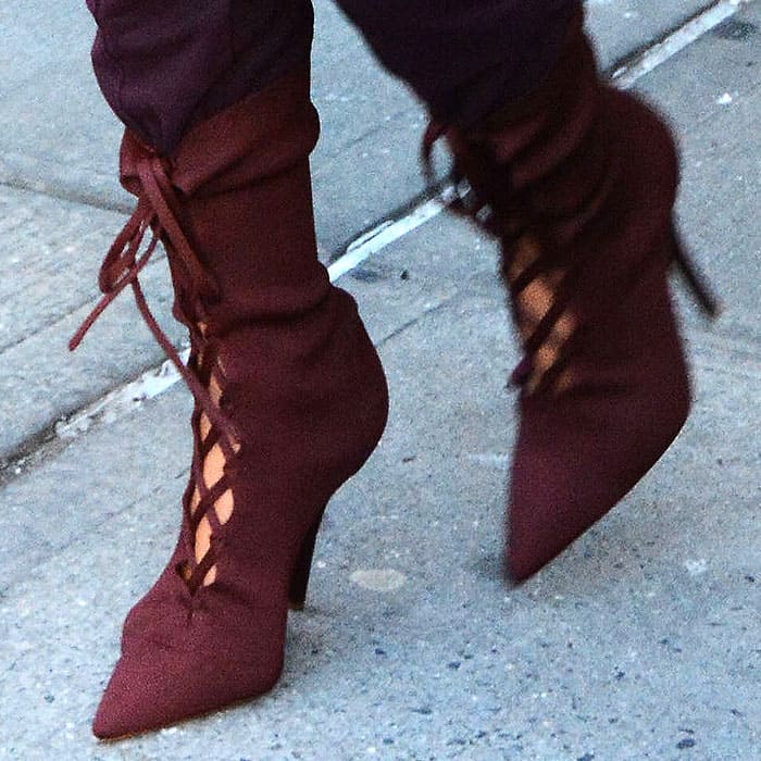 Kim Kardashian adds a rich pop of color with burgundy lace-up Yeezy ankle boots, featuring pointed toes, corset-inspired side lacing, and slim stiletto heels that echo the collection's streamlined, minimalist aesthetic