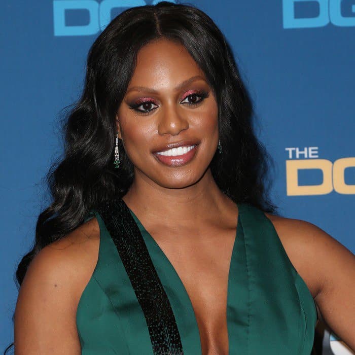Laverne Cox shines with a radiant smile, soft waves cascading over her shoulders, and a flawless display of natural, pearly teeth that perfectly complement her glamorous look