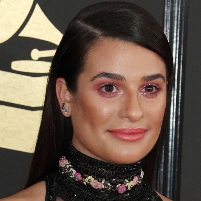 Lea Michele showcases sleek, straight hair with a center part, complemented by bold rose-gold smoky eyes and glossy peach lips