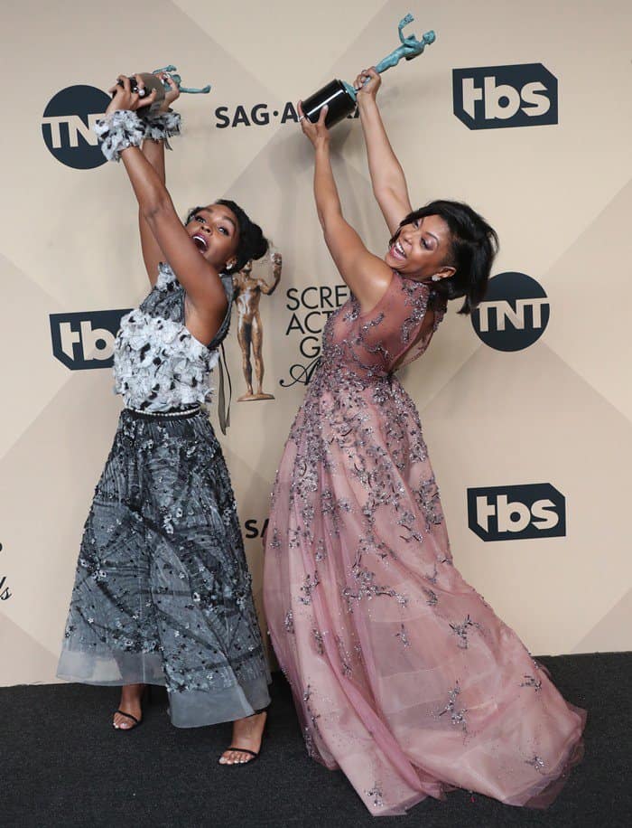 Janelle Monáe and Taraji P. Henson celebrated their SAG Awards win with playful energy, both lifting their trophies while stepping out in strappy black sandals—Taraji opting for sleek, minimalist heels with fine ankle straps that lengthened her silhouette beneath the flowing embellished gown, while Janelle’s barely-there sandals added a light, modern finish to her textured, tea-length ensemble