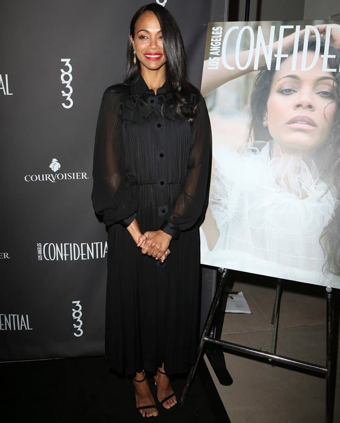 Zoe Saldaña stuns in a chic all-black ensemble featuring a sheer-sleeved Fendi midi dress and minimalist Jimmy Choo sandals, a look you can recreate by pairing a button-down midi dress with elegant ankle-strap heels