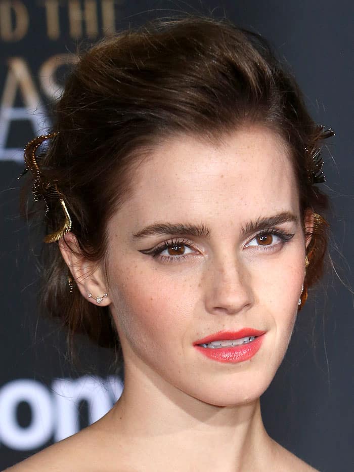 Emma Watson complements her striking red lip and natural makeup with a loose updo adorned with delicate gold leaf accents