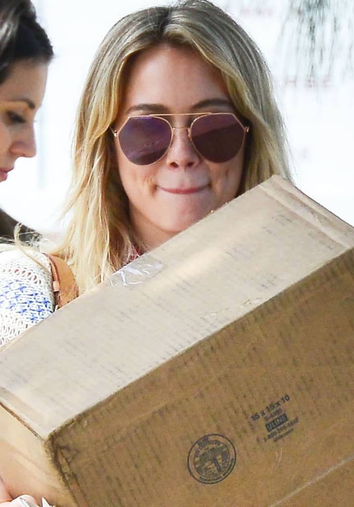 Hilary Duff carries a large package while wearing aviator sunglasses during a casual shopping outing