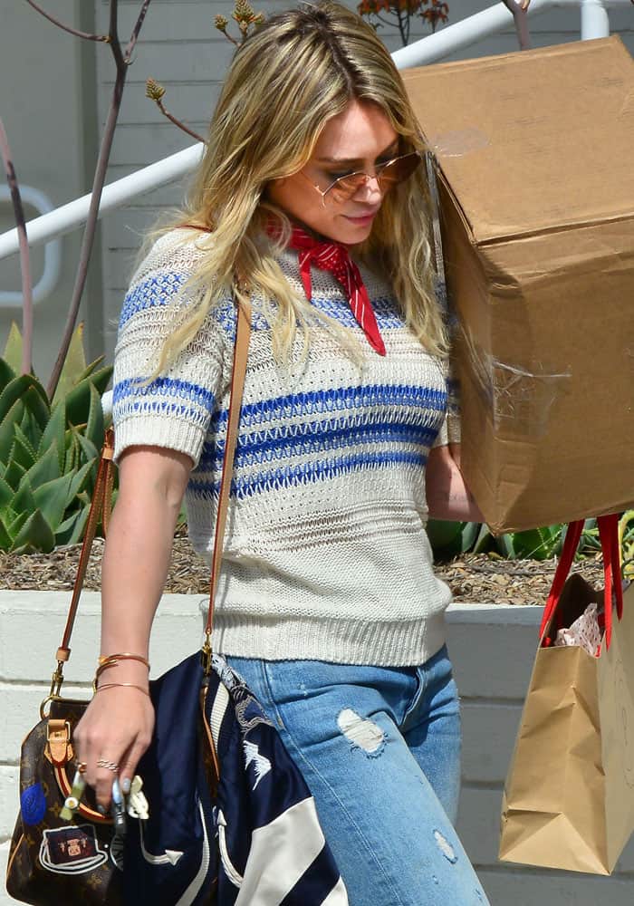 Hilary Duff balances a large package with effortless ease, pairing distressed skinny jeans, a striped knit sweater, and a red neck scarf