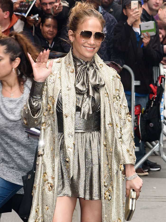 Jennifer Lopez sparkles in a matching Saint Laurent lamé pussy-bow blouse and metallic skirt coordinates, layered under a gold-embellished Jenny Packham coat