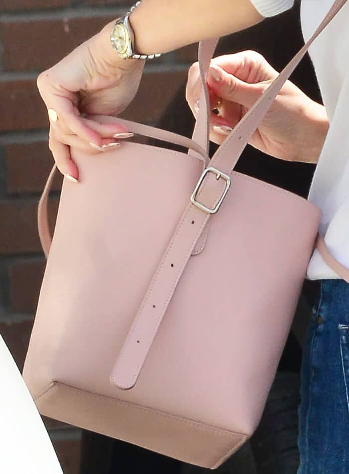 Reese Witherspoon rummages through her blush pink bucket bag—a sleek, structured accessory that complements her playful daytime look