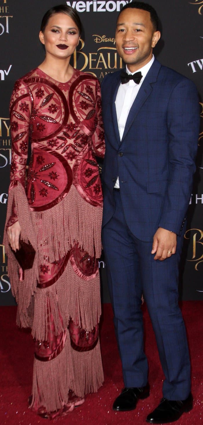 Chrissy Teigen stuns in a bold Raisa Vanessa gown with intricate embellishments and fringe, while John Legend complements her in a sleek navy tuxedo with a black bow tie