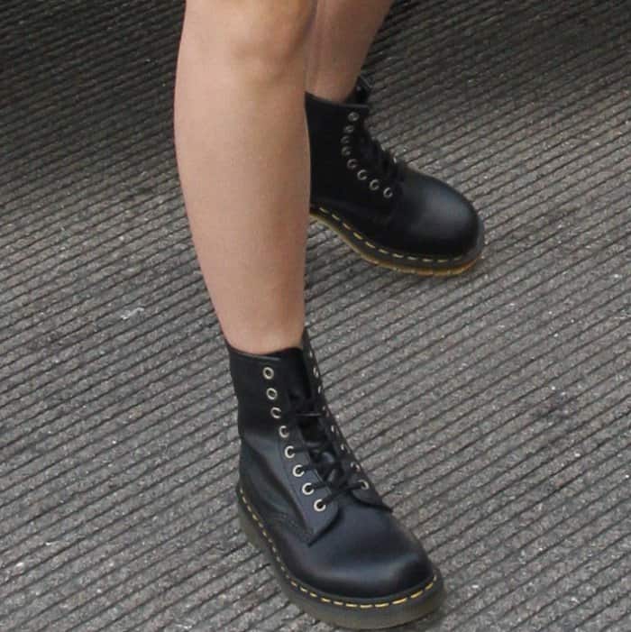 Emma Watson sports the iconic Dr. Martens '1460' boots, featuring smooth black leather, signature yellow stitching, and a sturdy Goodyear-welted sole—adding an effortlessly edgy touch to her travel-ready ensemble