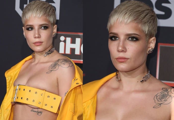 Close up, her platinum pixie cut and smoky eye makeup frame a cool, controlled expression, while the delicate choker and shoulder tattoo add contrast to the structured outfit