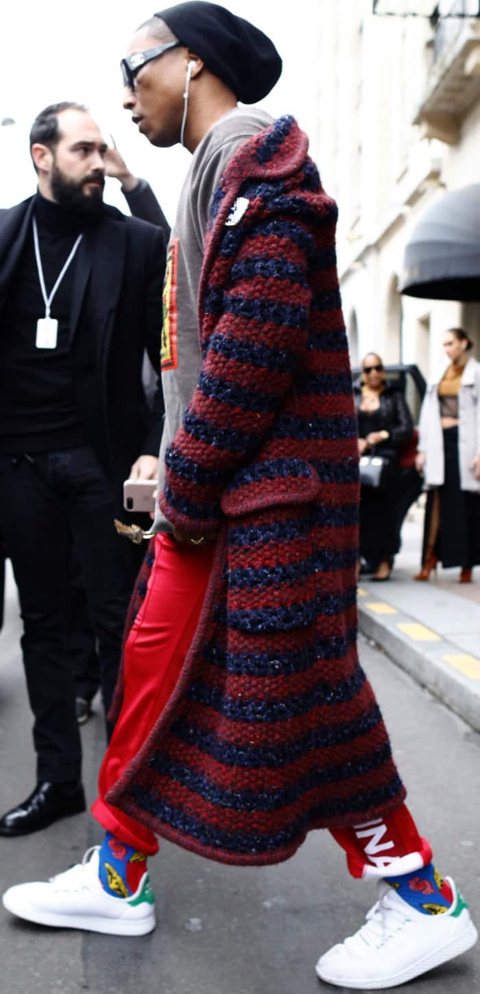 Pharrell Williams brings bold street-style energy in a striped Chanel knit coat, graphic tee, red track pants, colorful socks, and crisp white sneakers
