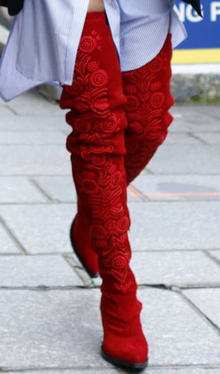 Rita Ora's striking red thigh-high boots feature intricate floral embroidery, adding a bold and textured statement to her Parisian street style