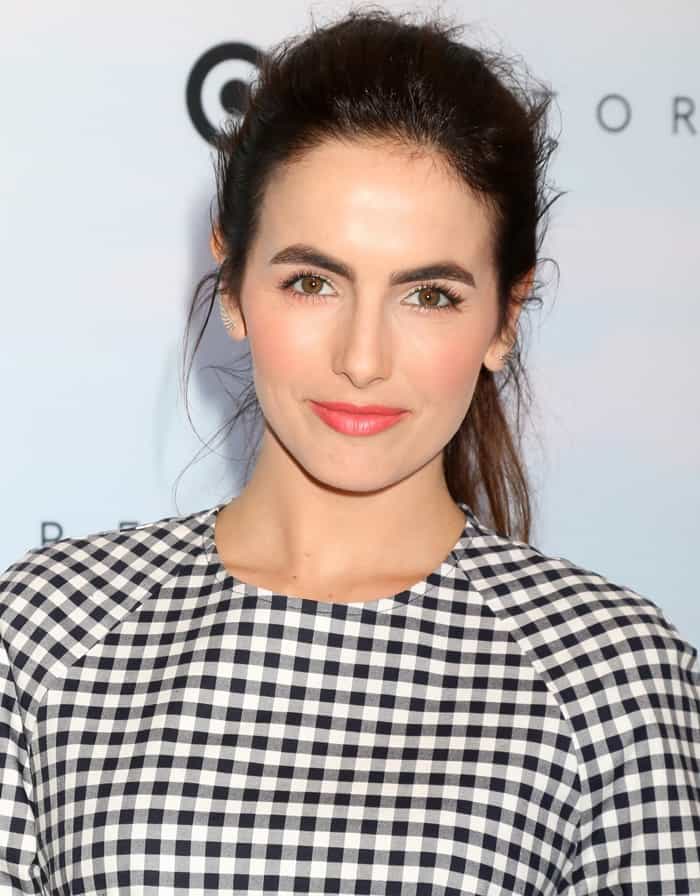 Camilla Belle showcases her radiant complexion with minimal makeup, perfectly highlighted by a vibrant coral lip that adds a fresh pop of color to her chic gingham outfit