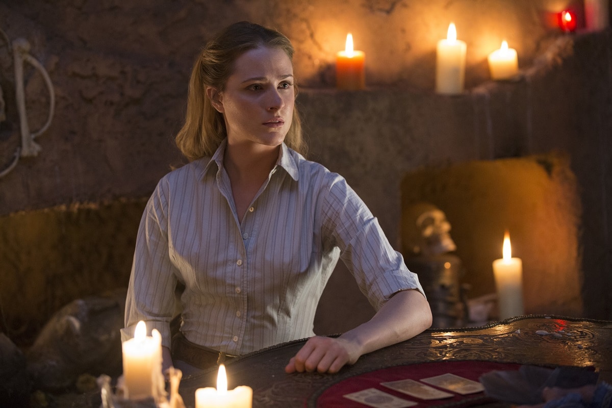 Evan Rachel Wood as Dolores Abernathy in Westworld, wearing a simple striped button-down shirt with rolled sleeves while surrounded by glowing candles in a tense scene