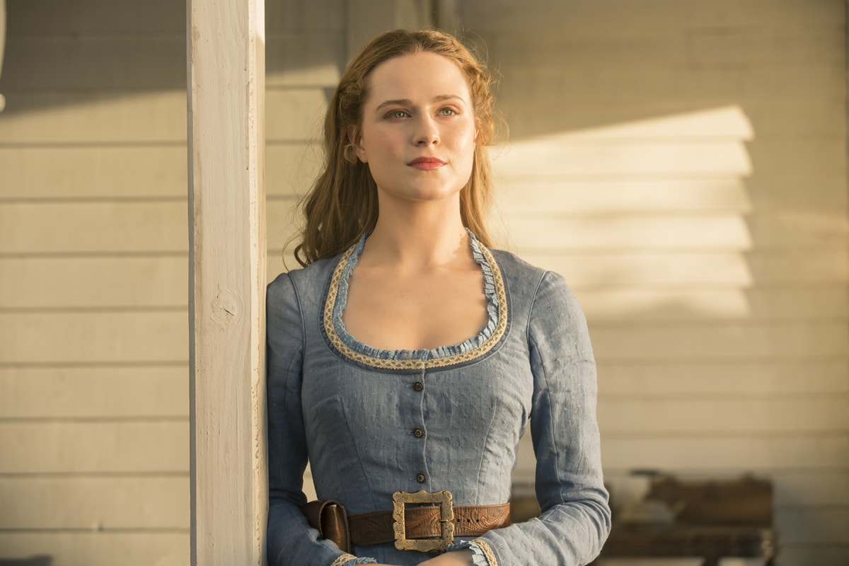 Evan Rachel Wood as Dolores Abernathy in Westworld, wearing a prairie-style blue dress with lace trim and a wide brown belt that reflects the show’s 1870s Western setting