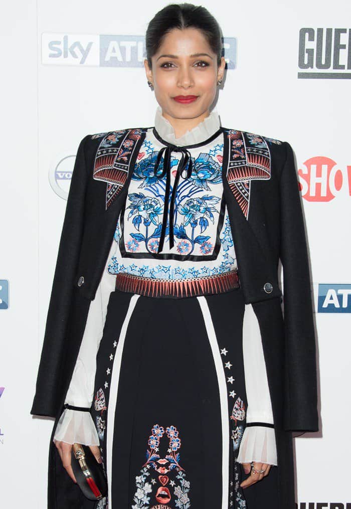 Freida Pinto stuns in an intricately embroidered ensemble featuring a structured jacket over a floral-patterned dress, complete with a bold red lip and sleek updo
