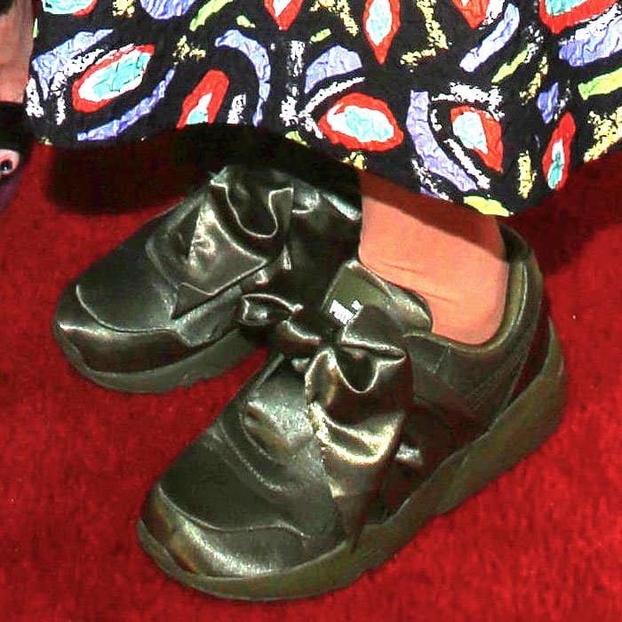 Close-up of Lena Dunham’s feet in olive green Fenty Puma by Rihanna Bow Sneakers, featuring satin uppers and oversized knotted bows for a bold statement look