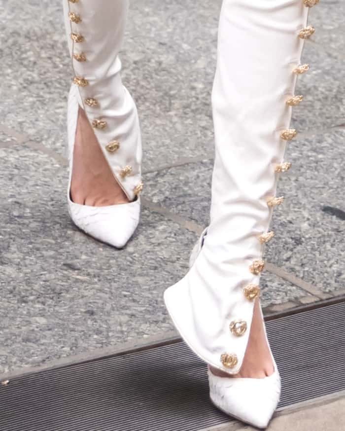 A close-up of Cara Delevingne’s custom white Olgana Paris pumps, perfectly framed by Redemption’s gold-buttoned split-hem pants for a bold, futuristic edge