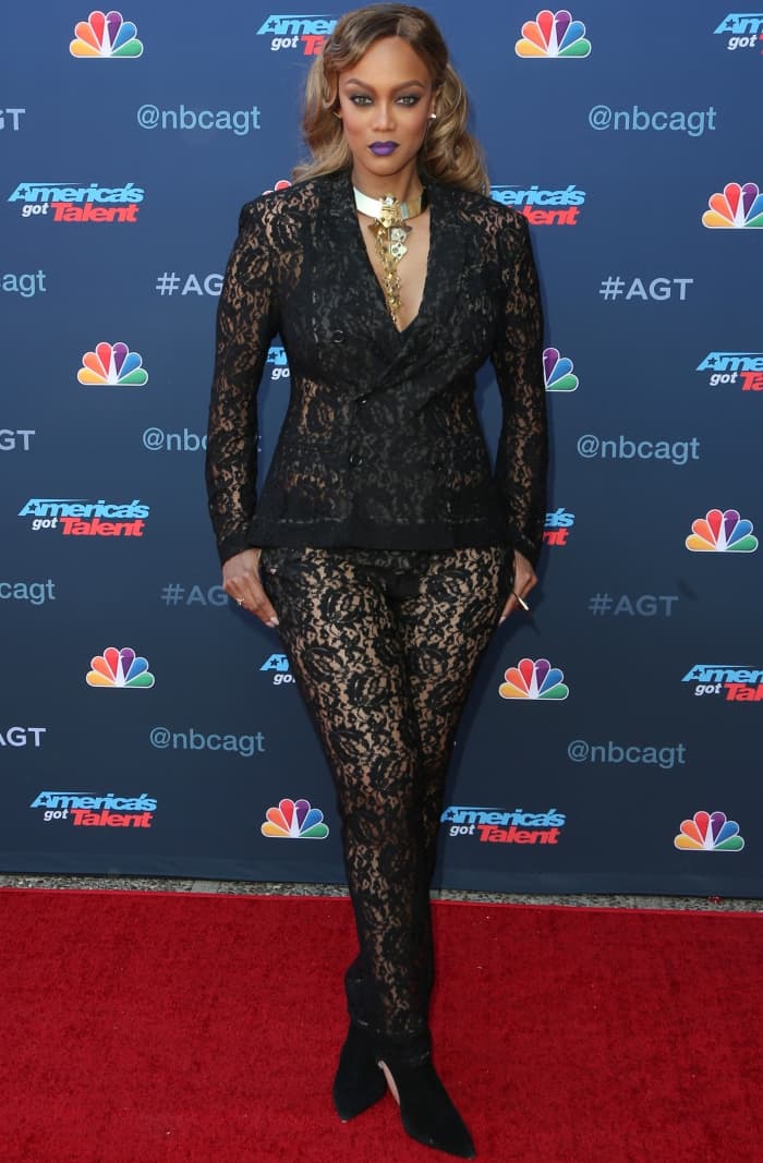 Tyra Banks arrives at the AGT Season 12 launch in a sheer black lace pantsuit styled with a sculptural gold statement necklace and pointed-toe cutout booties