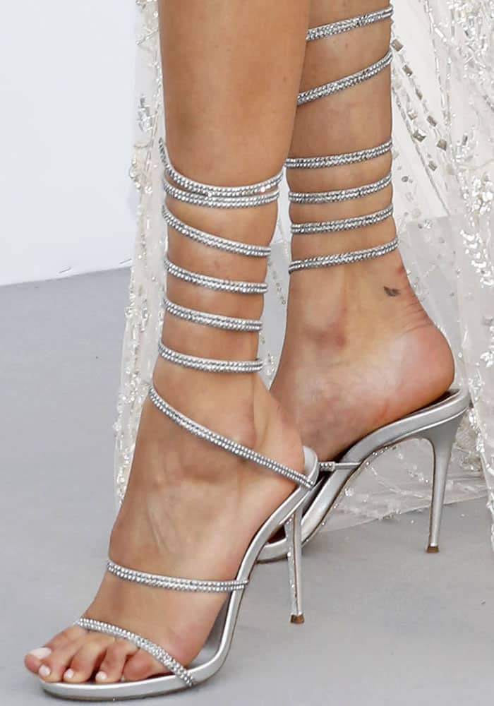 Bella Hadid stuns in René Caovilla silver gladiator sandals featuring crystal-embellished wraparound straps and a sleek stiletto heel for a dazzling red carpet finish