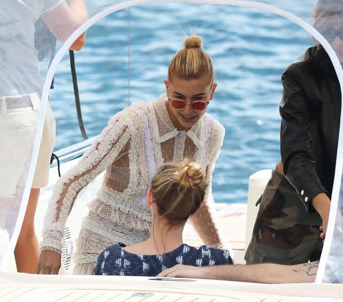 Hailey Baldwin wears tinted sunglasses and a sleek topknot bun while boarding a boat in Cannes, effortlessly blending chic accessories with her lace ensemble