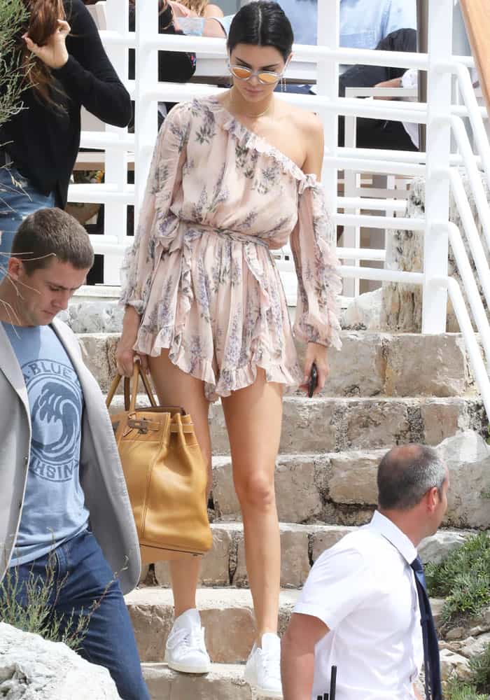 Kendall Jenner descends the steps in Cannes, effortlessly stylish in a floral Zimmermann romper, white Adidas 'Stan Smith' sneakers, and an oversized Hermès Birkin bag
