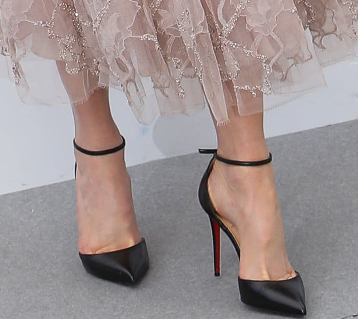 Pointed-toe black pumps with slim ankle straps add precision and contrast beneath the embroidered hem