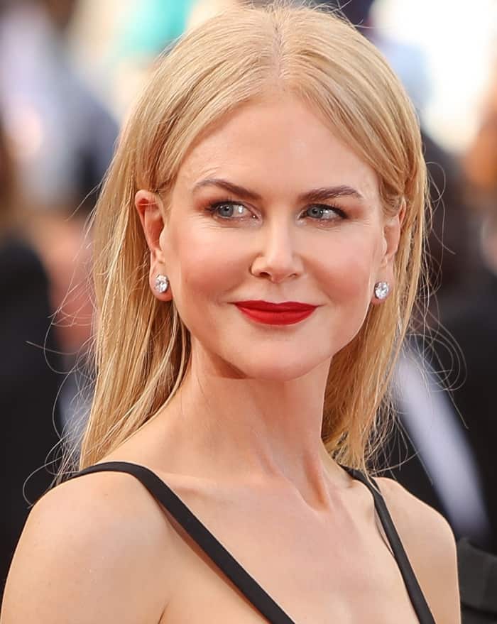 A sleek center-part, diamond studs, and bold red lipstick reinforce the clean lines